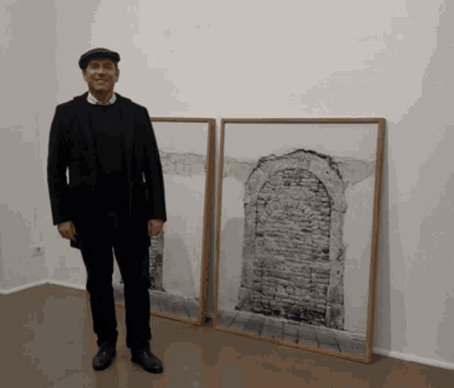 a man in a black suit stands in front of two framed pictures