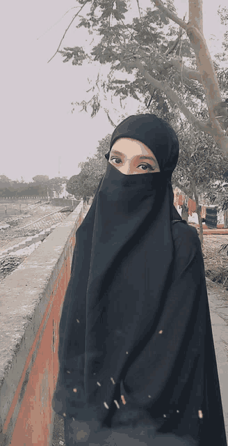 a woman wearing a black veil stands in front of a concrete wall