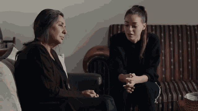 two women are sitting on a couch and talking