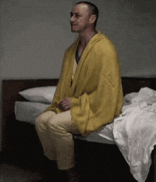 a man is sitting on a bed with a yellow blanket on him