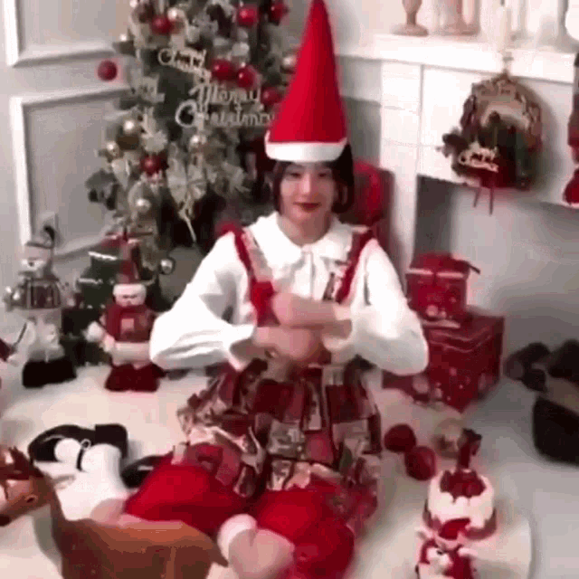 a woman wearing a santa hat is sitting in front of a christmas tree and a fireplace .