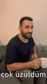 a man with a beard is sitting on a couch with a cup of coffee in his hand .