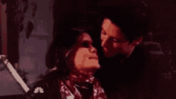 a man and a woman are kissing in a dark room . the woman is wearing a scarf .