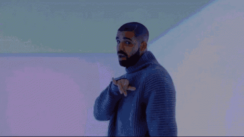a man with a beard is wearing a gray sweater and pointing at something .