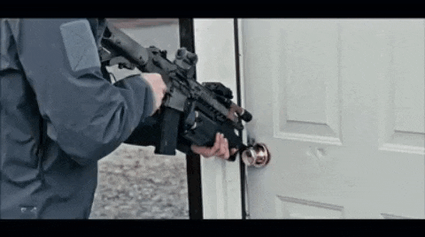 a man is holding a gun in his hand and opening a door .