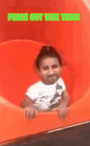 a little girl is sitting on an orange slide with the words peace out vibe tribe written above her