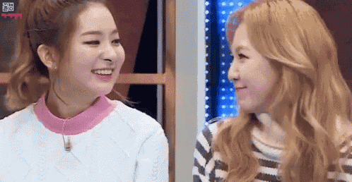 two women are looking at each other and smiling while sitting next to each other .