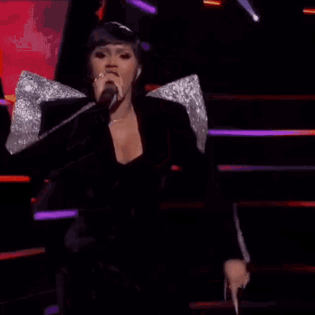 a woman is singing into a microphone on a stage while people applaud .