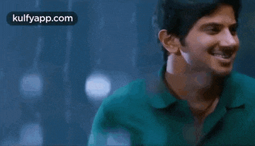 a man in a green shirt is smiling in the rain while wearing a green shirt .