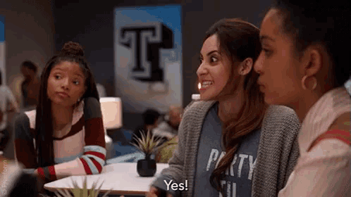 three women are sitting at a table talking to each other .