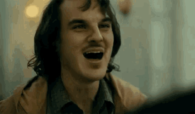 a man with a mustache is laughing with his mouth open in a close up of his face .
