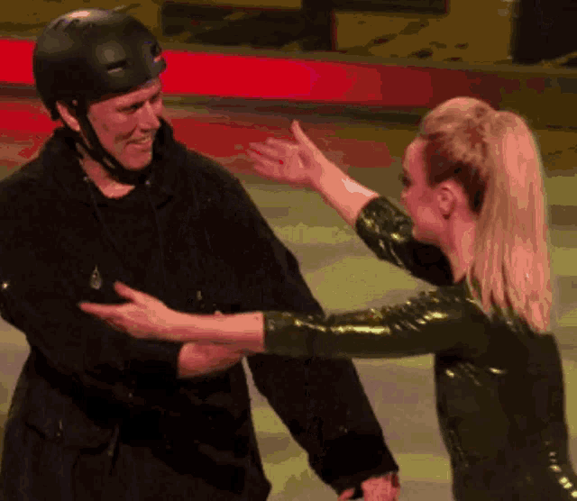 a man wearing a helmet is being hugged by a woman in a green outfit