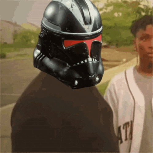 a man wearing a storm trooper helmet stands next to another man wearing a white shirt that says ath