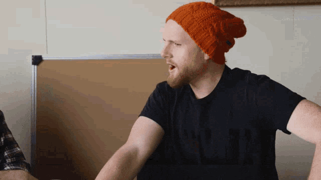 a man wearing an orange beanie and a black shirt is talking