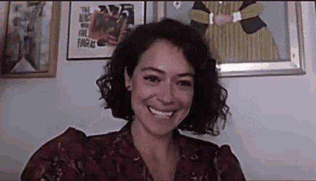 a woman with curly hair is smiling while sitting in front of a wall .