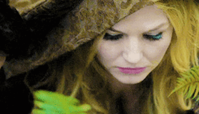a woman is wearing a hat and holding a green frog in her hand .
