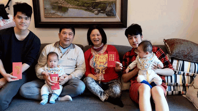 a group of people sitting on a couch holding red envelopes with chinese writing on them