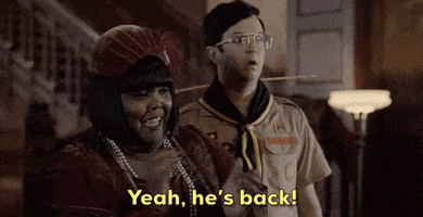 a man and a woman are standing next to each other and the man is saying yeah he 's back .