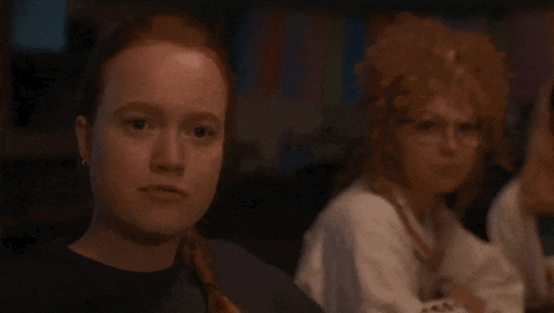 a woman with red hair and glasses is sitting next to a woman with blonde hair and glasses .