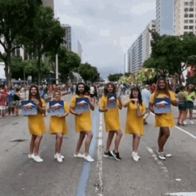 a group of women in yellow dresses are standing on a street holding signs