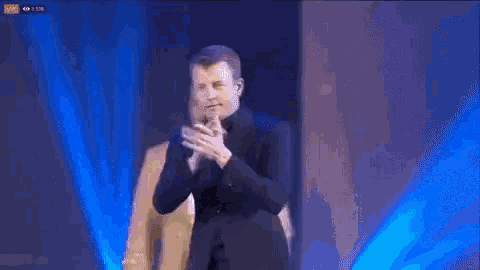 a man in a suit is clapping his hands on a stage
