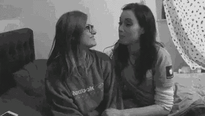 two women are sitting on a bed holding hands and kissing .