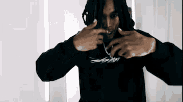 a man with dreadlocks is wearing a black hoodie and making a peace sign with his hands .