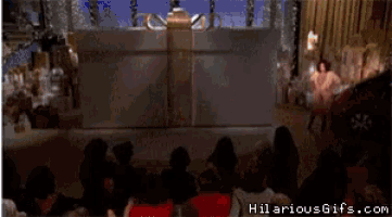 a group of people sitting in front of a stage with hilariousgifs.com on the bottom