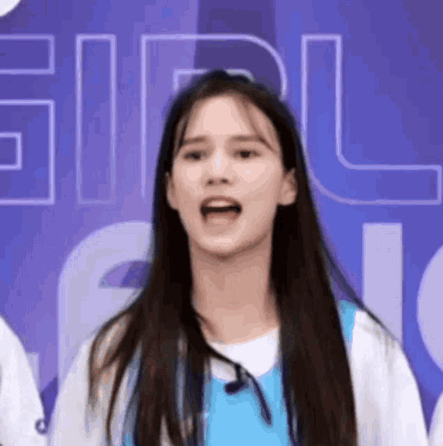 a girl with long hair is making a funny face in front of a blue wall .