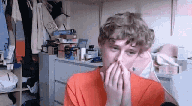 a young man with curly hair is covering his face with his hands