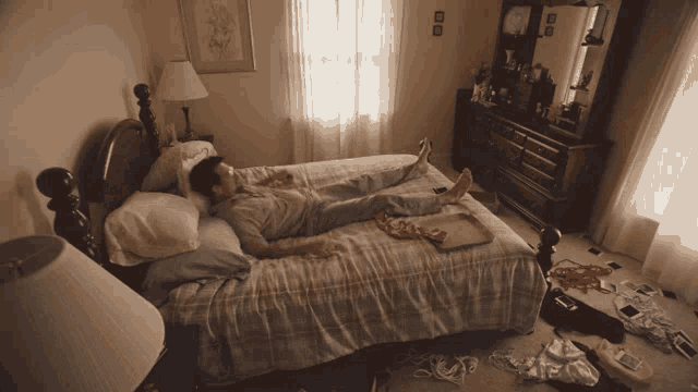 a man laying on a bed in a messy room with a tray of pizza on the bed