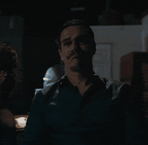 a man with a mustache looks at the camera in the dark