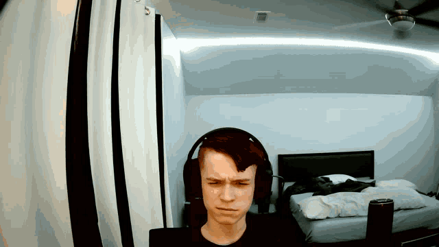 a young man wearing headphones in a bedroom with a ceiling fan