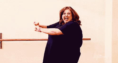a woman in a black shirt is standing in front of a ballet barre and screaming .