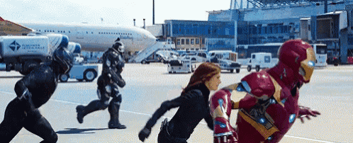a group of superheros are running on an airport runway in front of an airplane .