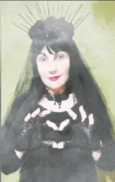 a woman in a black dress and veil is making a heart with her hands