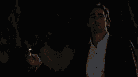 a man in a suit is standing in a dark room looking out a window .