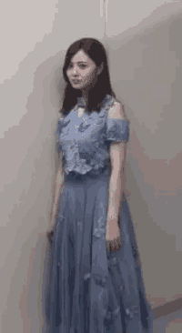 a woman in a blue dress is leaning against a wall and looking at the camera .