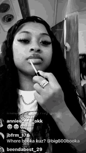 a black and white photo of a woman applying lip gloss on her lips