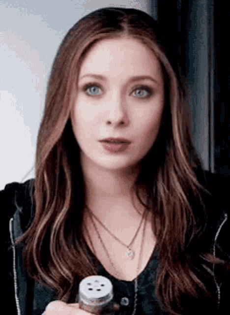 a woman with long brown hair and blue eyes is holding a salt shaker in her hand .