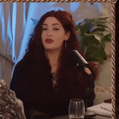 a woman with red hair is sitting in front of a microphone and a glass of water