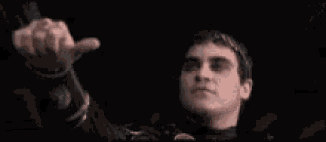 a man in a black suit is giving a thumbs up sign in the dark .