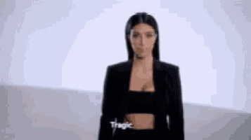 a woman in a black jacket and black top is standing in front of a white wall .
