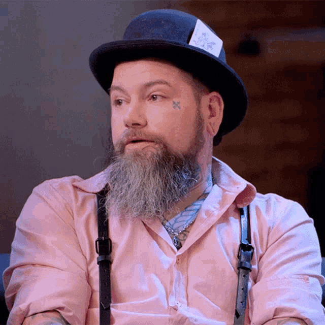a man with a beard is wearing a pink shirt and a hat