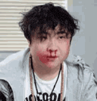 a man with a bloody nose is wearing a necklace and a t-shirt .