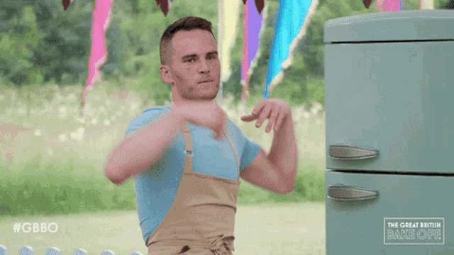 a man with his arms outstretched in front of a green refrigerator that says gbbo