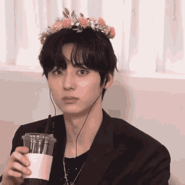 a young man with a flower crown on his head is drinking a cup of coffee