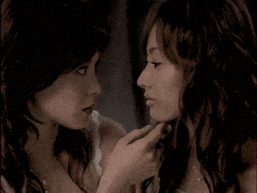 two women are touching each other 's faces in a dark room
