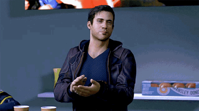 a man in a brown jacket stands in front of a shelf with a box of waffle donuts on it