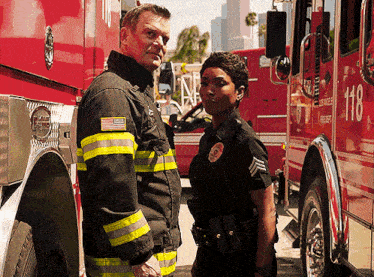 a man and a woman are standing in front of a red fire truck with the number 118 on it
